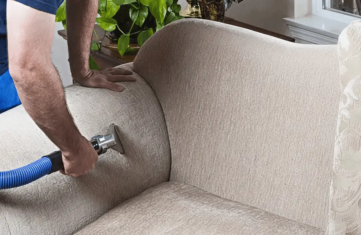 Professional upholstery cleaner deep-cleaning a fabric sofa with a handheld extraction tool and hose, Oakland, CA.